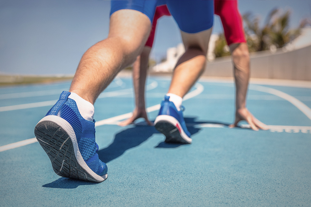 A person at the starting line of a track, with the image focused on the person's blue running shoes made from supercritical foam.