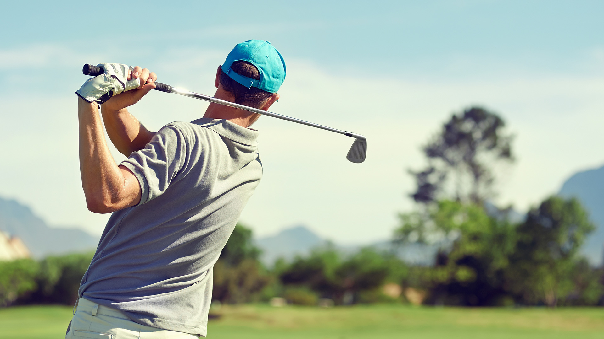 How ProvenComfort Makes Building Shoes Easy A back view of a golfer taking a large swing on a course with a line of trees and mountains in the background.