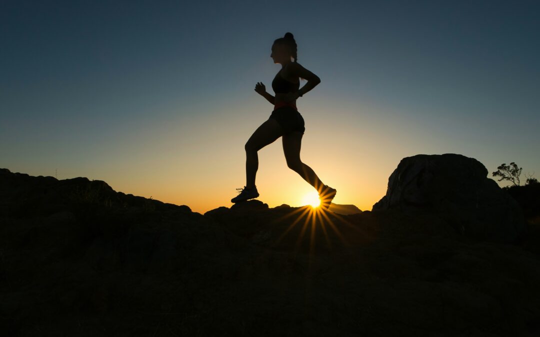 The silhouette of a woman who is trail running at sunset